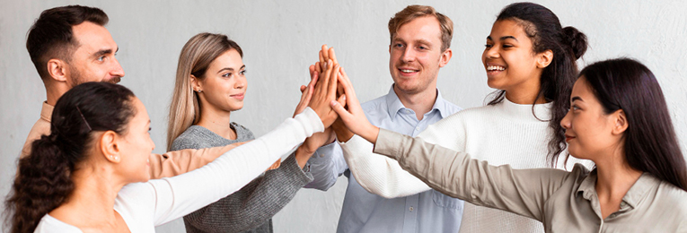 Image showing several corporate workers, including men and women, standing in a huddle and joining their hands in the centre.