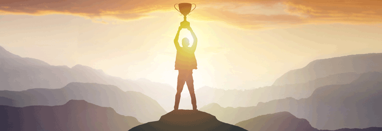 a person standing on a hill top and holding a trophy by stretching his hands over his head