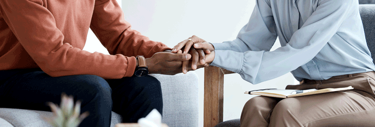 A person with a book on their lap, holding another person's hands.