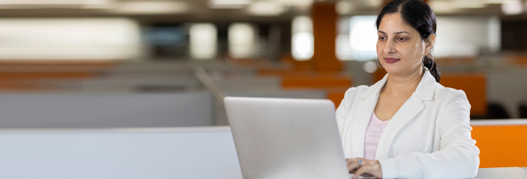 A woman in a full white formal outfit working on her laptop at her workspace.
