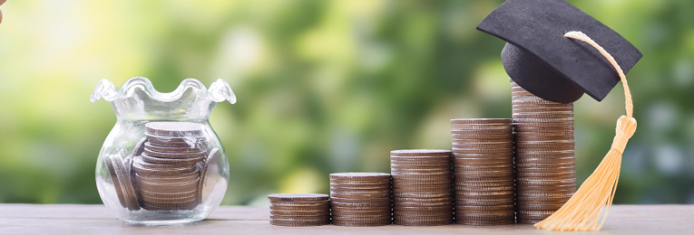 A jar filled with coins sits next to a row of dollar coins arranged in ascending order, with a graduation cap placed on the highest step.
