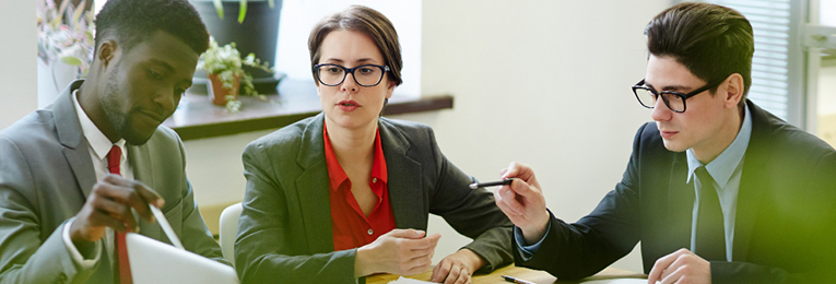 Three people engaged in a discussion, referring to a laptop on the meeting table.