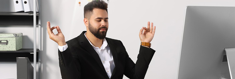 A person sitting in a yoga pose at their work desk, with both hands raised in the air.