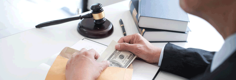 A person is seen taking a stack of dollar bills from a brown cover, with a gavel resting on the table opposite them.