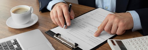 A midsection view of a person examining a form, holding a pen in one hand while the other traces the document.
