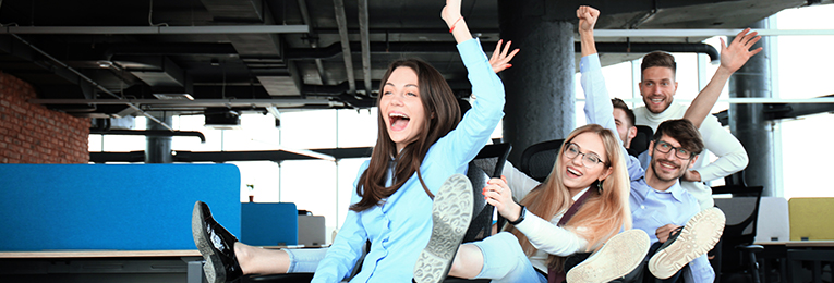 Image showing a group of people, both men and woman who appear to be coworkers, exult in happiness. They are throwing their arms and legs in the air to show joy.